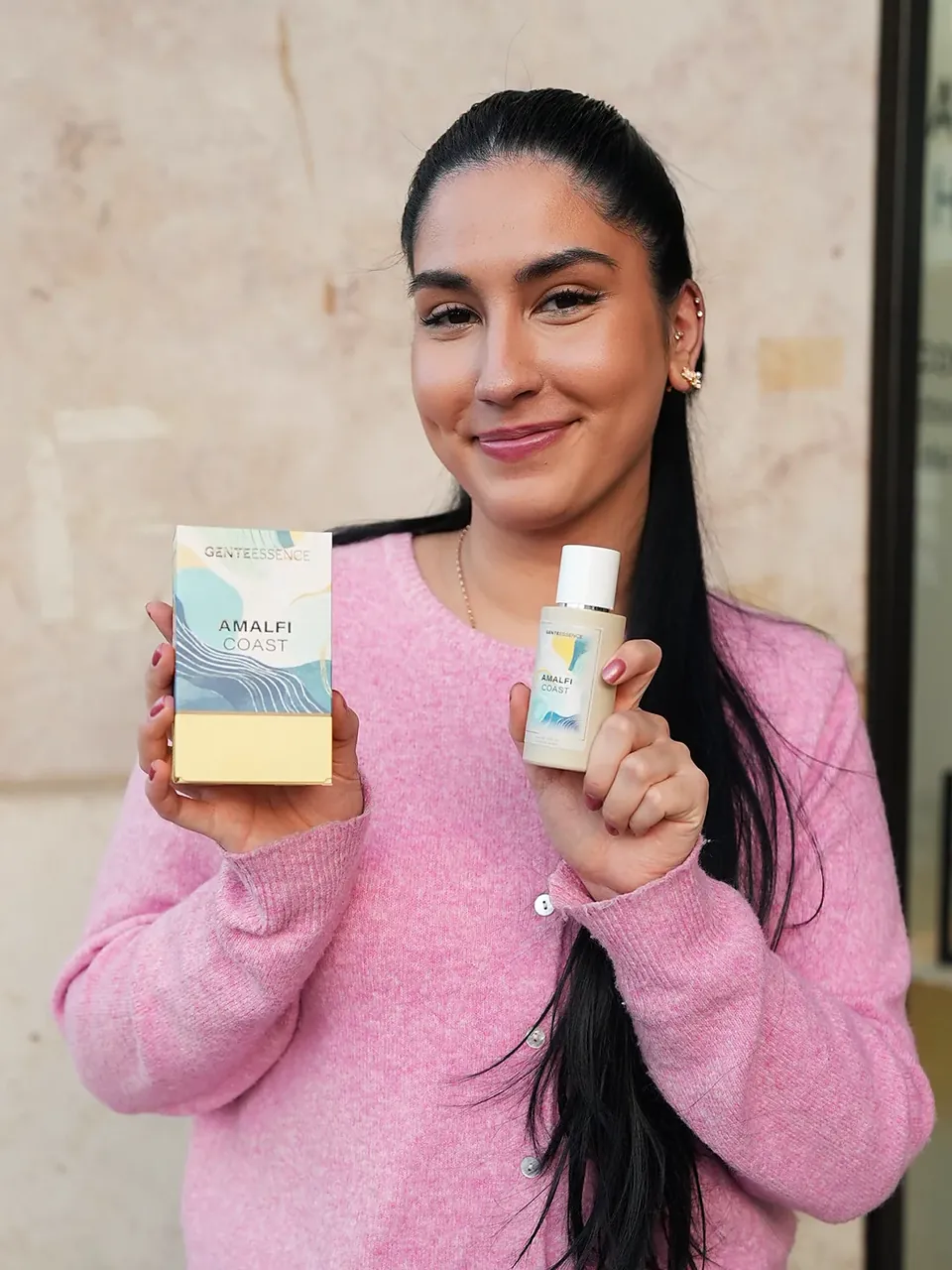 Amalfi Coast: Eine Frau mit langem schwarzem Zopf und rosa Strickjacke hält Verpackung und Flakon. Originalfoto.